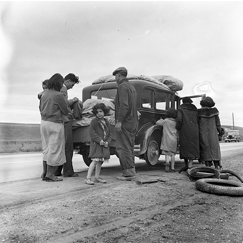 Historical photo of a Mexican family standing by car near side of the road.