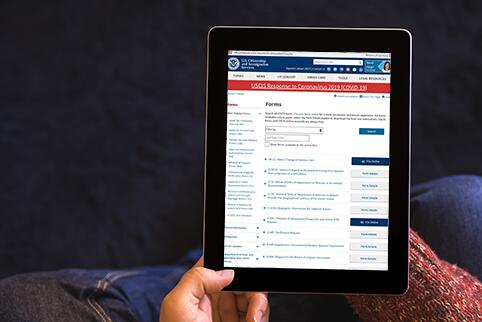Picture of a person holding a tablet with a list of USCIS forms on the screen