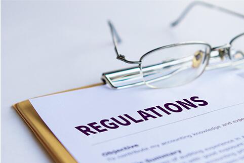 Clipboard with a paper on it that says Regulations. A pair of glasses are sitting on the clipboard.